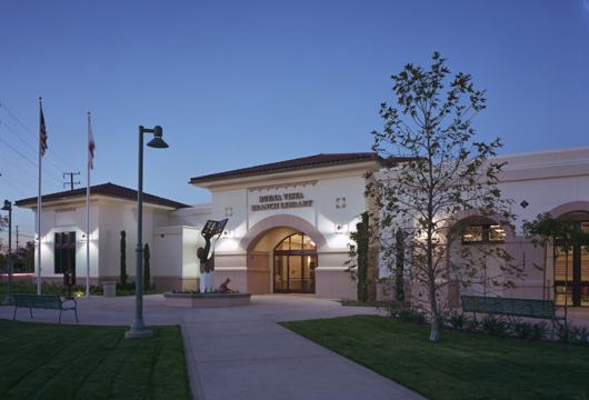The Buena Vista Branch Library at dusk, with flags, lights, benches, and a tree in front.