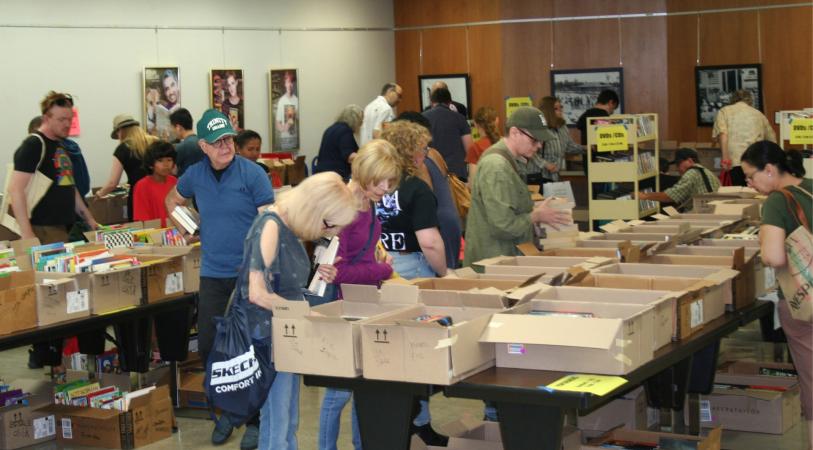 people of all ages going through boxes of used books at a book sale in a library auditorium