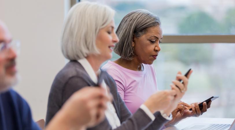 Three older adults looking at their phones in a brightly lit room.
