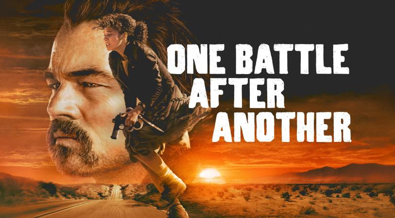 Promotional poster for “One Battle After Another” shows a large close-up of a stern, bearded man behind a running figure in a desert at sunset, with tense, cinematic tones.