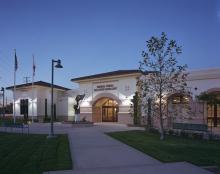 The Buena Vista Branch Library at dusk, with flags, lights, benches, and a tree in front.